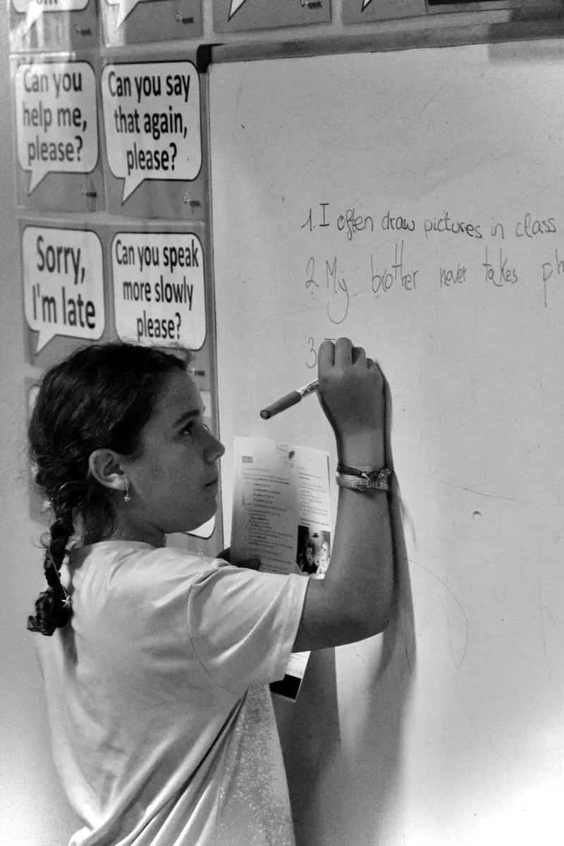 Alumna adolescente escribiendo en inglés en la pizarra